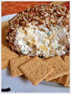 a white plate topped with crackers and a cheese ball covered in nuts on top of tortilla chips