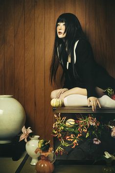 a woman sitting on top of a wooden table next to vases and other items