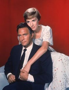 a man sitting next to a woman on top of a couch in front of a red wall