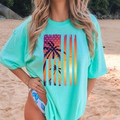 "🌅 Embrace the Perfect Blend of Patriotism and Beachside Bliss with Our \"Beach Sunset American Flag\" Oversized Tee! 🏖️🌴 Introducing a tee that seamlessly merges the iconic American USA flag with the enchanting allure of a tropical sunset - the \"Beach Sunset American Flag\" oversized beach tee. It's designed for those who cherish the spirit of the stars and stripes and the tranquility of coastal paradise. 🌅 A Sunset of Freedom and Serenity 🌞 At the heart of this tee is a retro neon Americ Blue Palm Tree Print Tops For Beach Season, Green Beach Tops For Beach Season, Blue Hawaiian T-shirt For Beach, Green Beachwear Tops For Beach Season, Blue Hawaiian T-shirt With Crew Neck, Green Short Sleeve Beachwear Top, Green Short Sleeve Tops For Beach Season, Green Tops For Beach Season, Blue Hawaiian Crew Neck T-shirt