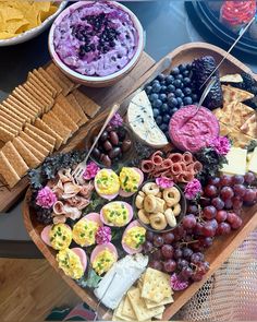 an assortment of cheeses, crackers and grapes on a platter