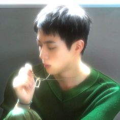 a young man wearing a green sweater is holding something in his hand and looking at it