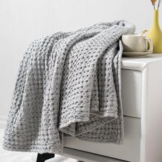 a gray blanket sitting on top of a white dresser next to a cup and vase