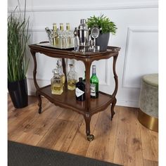 an old fashioned bar cart with liquor bottles and glasses on the shelf next to a potted plant