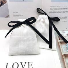 two white bags with black ribbon tied around them on top of a table next to an open book