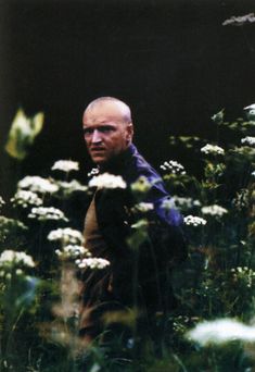 a man standing in the middle of a field of flowers with his head turned to the side