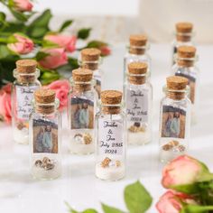 six small bottles filled with sand next to pink roses and greenery on a table