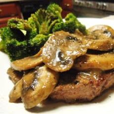 a white plate topped with meat covered in mushrooms and broccoli