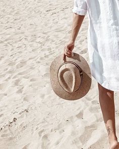 a person walking on the beach with a hat