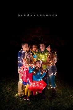 a group of people standing next to each other in the grass with lights on them