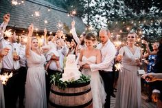 a group of people standing around a cake on top of a barrel with sparklers