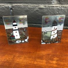 two small glass plaques with lighthouses on them sitting on a wooden table next to a brick wall