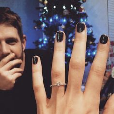 a woman with black nails and a ring on her finger next to a christmas tree