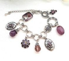 Adorn your wrist with this gorgeous vintage-inspired charm bracelet! Made to look stylish and feel fabulous, this lovely piece of jewellery teams a charm bracelet aesthetic with a chain link design. There is a purple rectangle-shaped charm with crystals, 2 oval shape pendants with crystals a capped teardrop glass amethyst bead adorned with tiny crystals, a purple flower charm with pink crystal centre, a capped faceted light purple acrylic bead, a round link with a crystal centre, a larger link w Vintage Purple Metal Bracelets, Handmade Vintage Purple Bracelets, Charm Bracelet Aesthetic, Bracelet Aesthetic, Purple Acrylic, Link Design, Bracelet Crystal, Glass Charms, Bracelet Chain