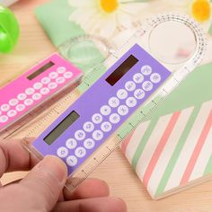 a hand holding a purple calculator next to a pink and green plastic ruler