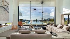 a living room filled with lots of furniture and large windows overlooking a lake in the distance