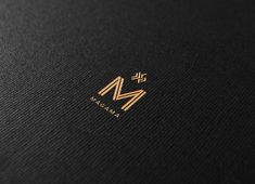 the letter m is inscribed in gold on black paper