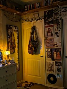 a yellow door in a small room with posters on the wall and a purse hanging from it's handle