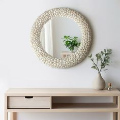 a table with a mirror, vase and plant on it in front of a white wall