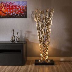 a tall metal sculpture sitting on top of a wooden floor next to a painting and lamp