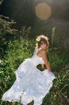 a woman in a white dress is sitting on the grass and posing for a photo