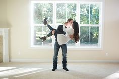 a man holding a woman in his arms while standing in front of a large window