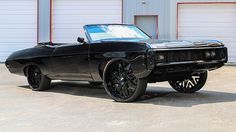 a black muscle car parked in front of a garage