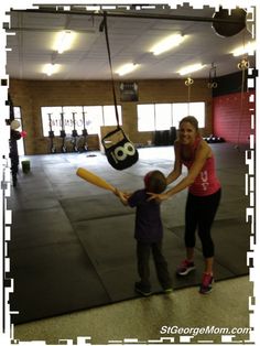 a woman teaching a child how to swing a baseball bat in a gym with the number 50 on it