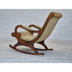 a wooden rocking chair with beige upholstered seat and foot rest, in front of a white brick wall