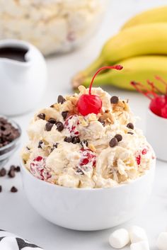 an ice cream sundae with chocolate chips and cherries in a bowl next to bananas