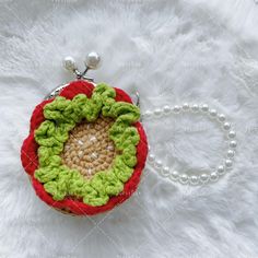 a crocheted red and green purse on a white furnishing with pearls