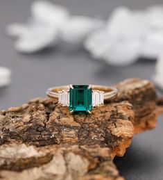 an emerald and diamond ring sitting on top of a rock