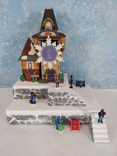 a small clock tower with people around it and snowing on the ground behind it