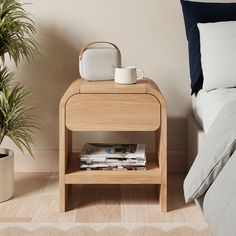 a small wooden table next to a bed with a plant on it and a mug