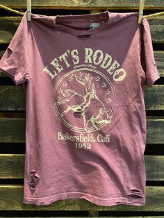 Country Deep Let's Rodeo Bakersfield 1980's Distressed Unisex T shirt vintage wash berry Throw back vintage tee from 1980's 40 Singles Jersey 100% Cotton Premium quality ringspun and compacted cotton Fine Cotton Jersey that is pigment dyed for a more vintage look Features tears and destroyed features at neck and on body Each piece is unique as this process is done by hand! 3.8 oz Made In USA Every garment dye item can be a slightly different shade in color since this is a laundry dye process. En Bakersfield California, Distressed Tee, Linen Style, Unique Designers, Online Tops, Vintage Tees, Cotton Tops, Vintage Look, Rodeo