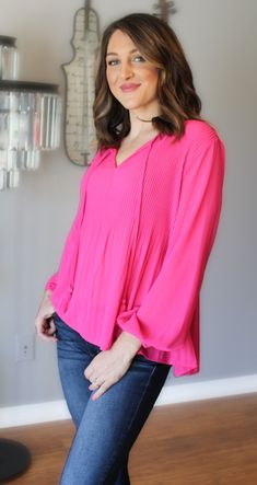 Looking for something pretty, breezy and whimsical? This is the blouse for you! This pink beauty is loose fitting, light weight and fun. The delicate pleated detail is on the front and back and tapers off near the waist. The long sleeves have an elastic cuff and the front is enhanced with the most adorable fringe tie neck. The vibrancy of the pink is nothing short of stunning. Color: Hot Pink Pleated Upper Torso Elastic Cuffs Slightly Longer Back Hem Fringed Neck Tie True to Size Yet Loose Fitti Spring Pleated V-neck Blouse, Pleated V-neck Blouse For Spring, Chic Pink Tops With Balloon Sleeves, Chic Pink Balloon Sleeve Tops, Chic Balloon Sleeve Long Sleeve Top For Spring, Chic Long Sleeve Balloon Sleeve Top For Spring, Chic Long Sleeve Balloon Top For Spring, Pink Balloon Sleeve Tops For Day Out, Casual Pink Top With Blouson Sleeves