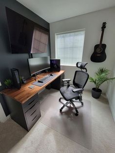 a computer desk with a guitar hanging on the wall next to it and a chair