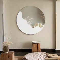 a round mirror hanging on the wall above a table with candles and a blanket in front of it