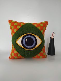 a decorative pillow with an eye on it next to a black vase and pen holder