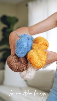 three skeins of yarn are being held by someone's hands in front of a white couch