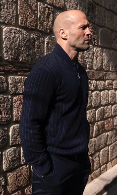 a bald man standing in front of a brick wall