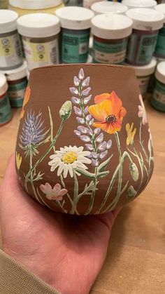 a hand holding up a painted vase with flowers on it