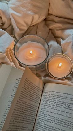 an open book sitting on top of a bed next to two lit candles in a glass bowl