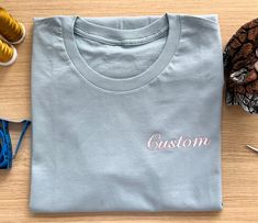 100% Cotton Tshirt . Please Choose Color Font and Name so we can make it. Basic Relaxed Fit Top With Custom Embroidery, Basic Cotton Tops With Custom Embroidery And Relaxed Fit, Casual Crew Neck T-shirt With Custom Embroidery, Cotton T-shirt With Embroidered Text, Crew Neck, Cotton T-shirt With Embroidered Graphics, Crew Neck, Blue Crew Neck T-shirt With Embroidered Text, Blue Crew Neck Top With Custom Embroidery, Blue Relaxed Fit T-shirt With Embroidered Text, Cotton T-shirt With Embroidered Graphics And Crew Neck