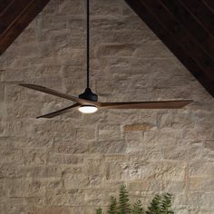 a ceiling fan mounted to the side of a stone wall next to a potted plant