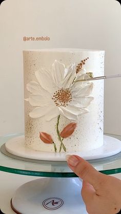 a hand is pointing at a white cake with flowers on it