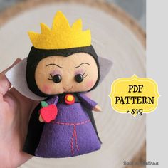 a hand holding a small doll with a crown on it's head and wearing a purple dress