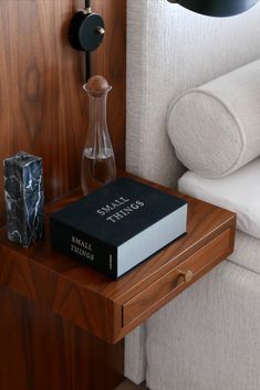 a book sitting on top of a wooden table next to a white chair and lamp