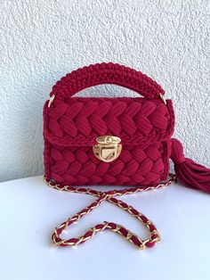 a red handbag sitting on top of a white table next to a chain strap