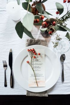 a place setting with silverware, napkins and red berries on the dinner table